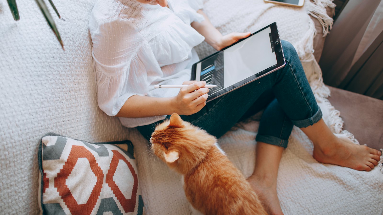 A woman resting on a sofa with a tablet, a cat beside her