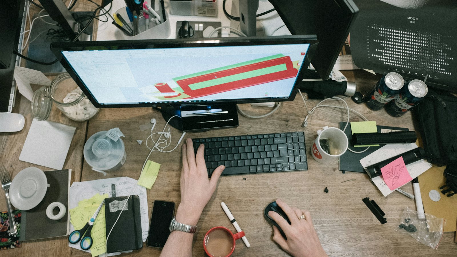 A cluttered desk with a computer, notes and a person typing