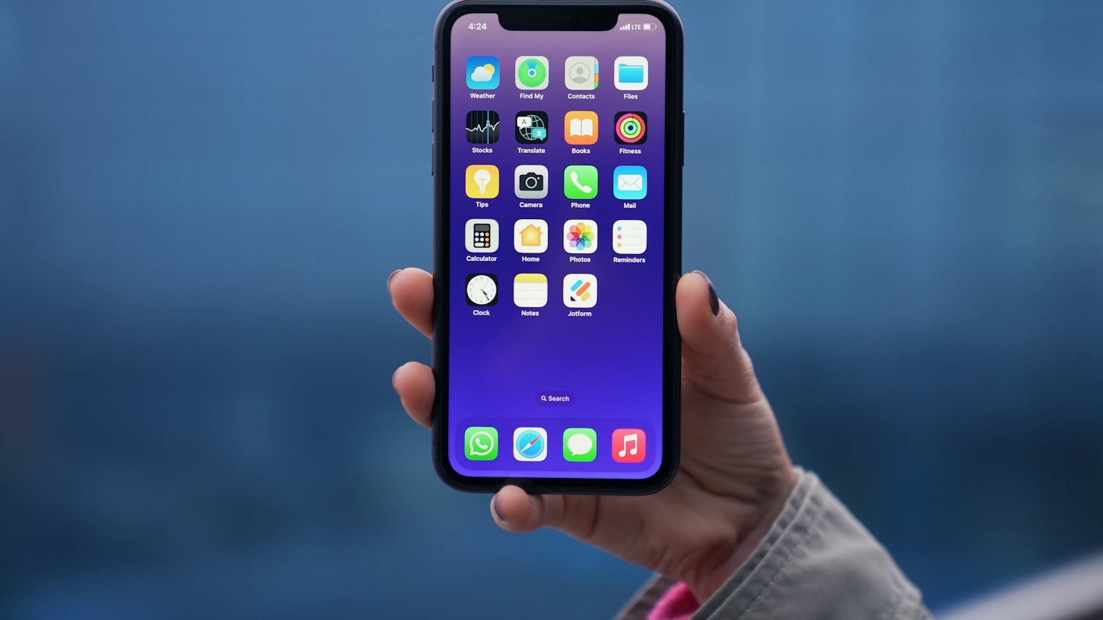 A hand holding a smartphone showing its home screen