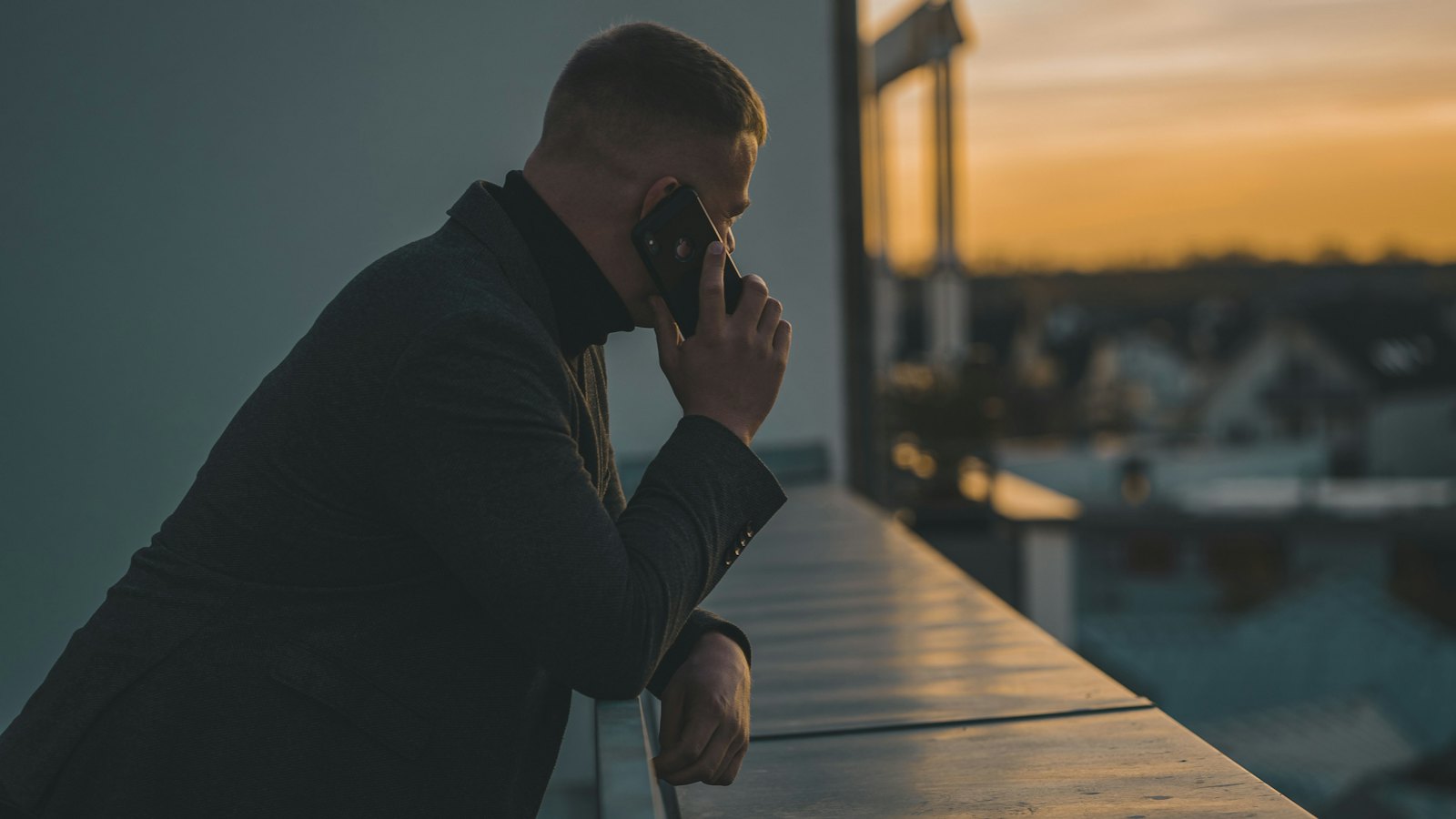 A man on a phone call leaning by a window at sunset