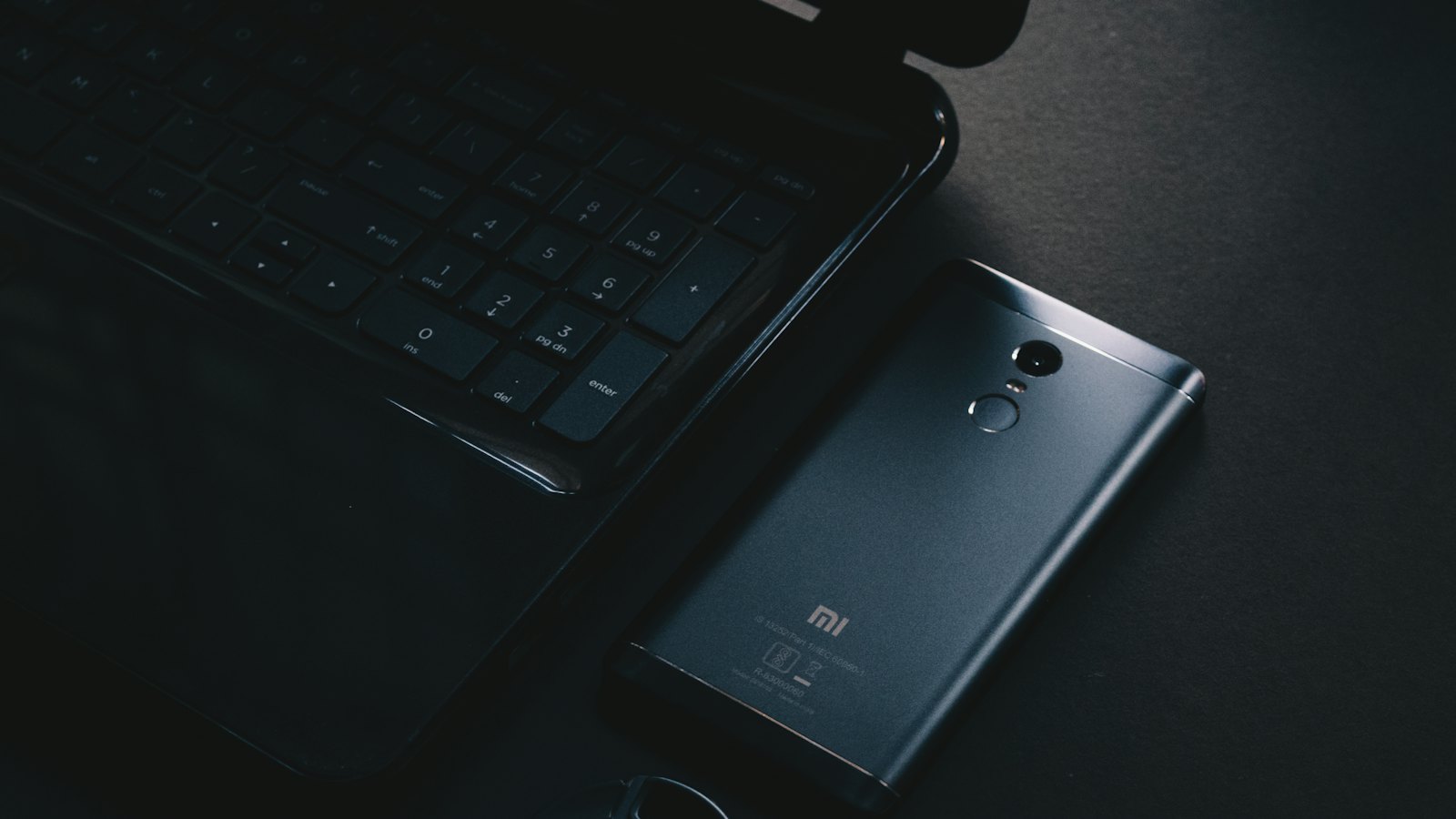 A phone lying beside a laptop keyboard on a dark desk