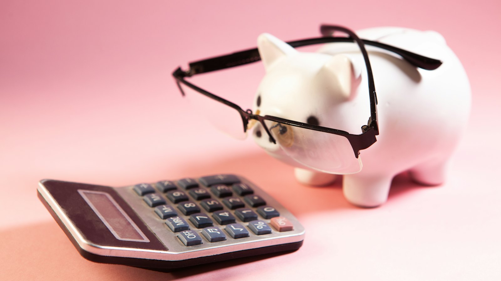 A piggy bank wearing glasses next to a calculator