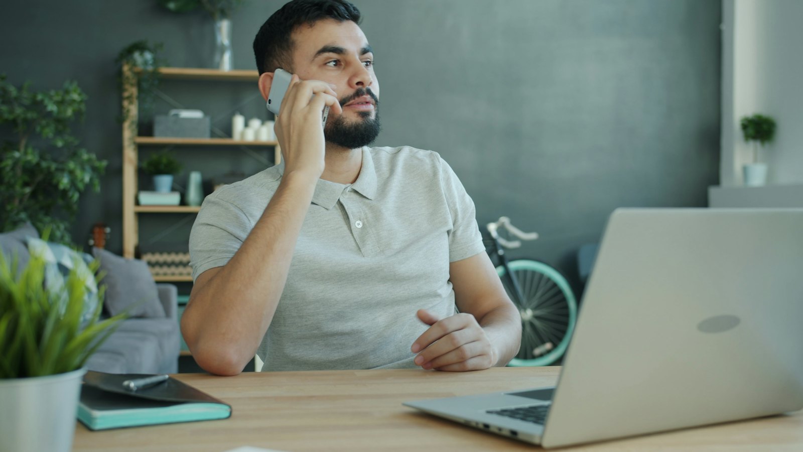 A man on a phone call at a desk with his laptop