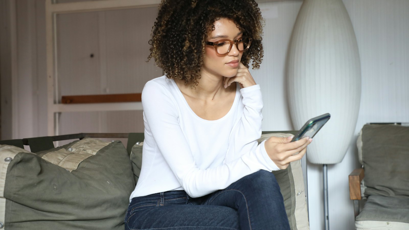 A woman sitting on a sofa looking at her phone with a worried expression