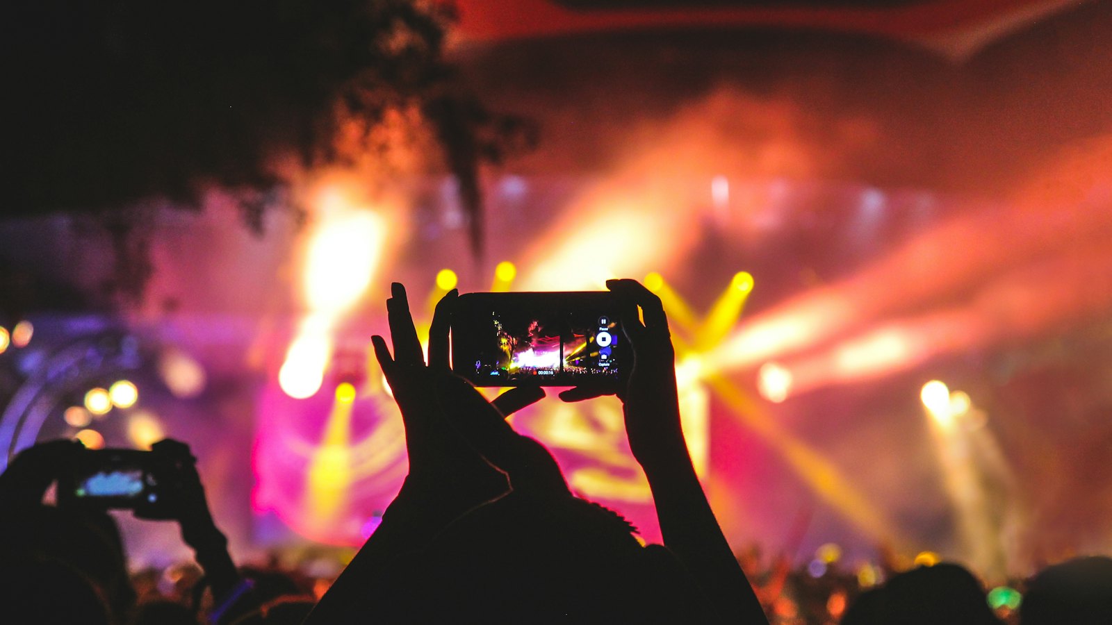 A fan holding up a phone to film a brightly lit concert stage