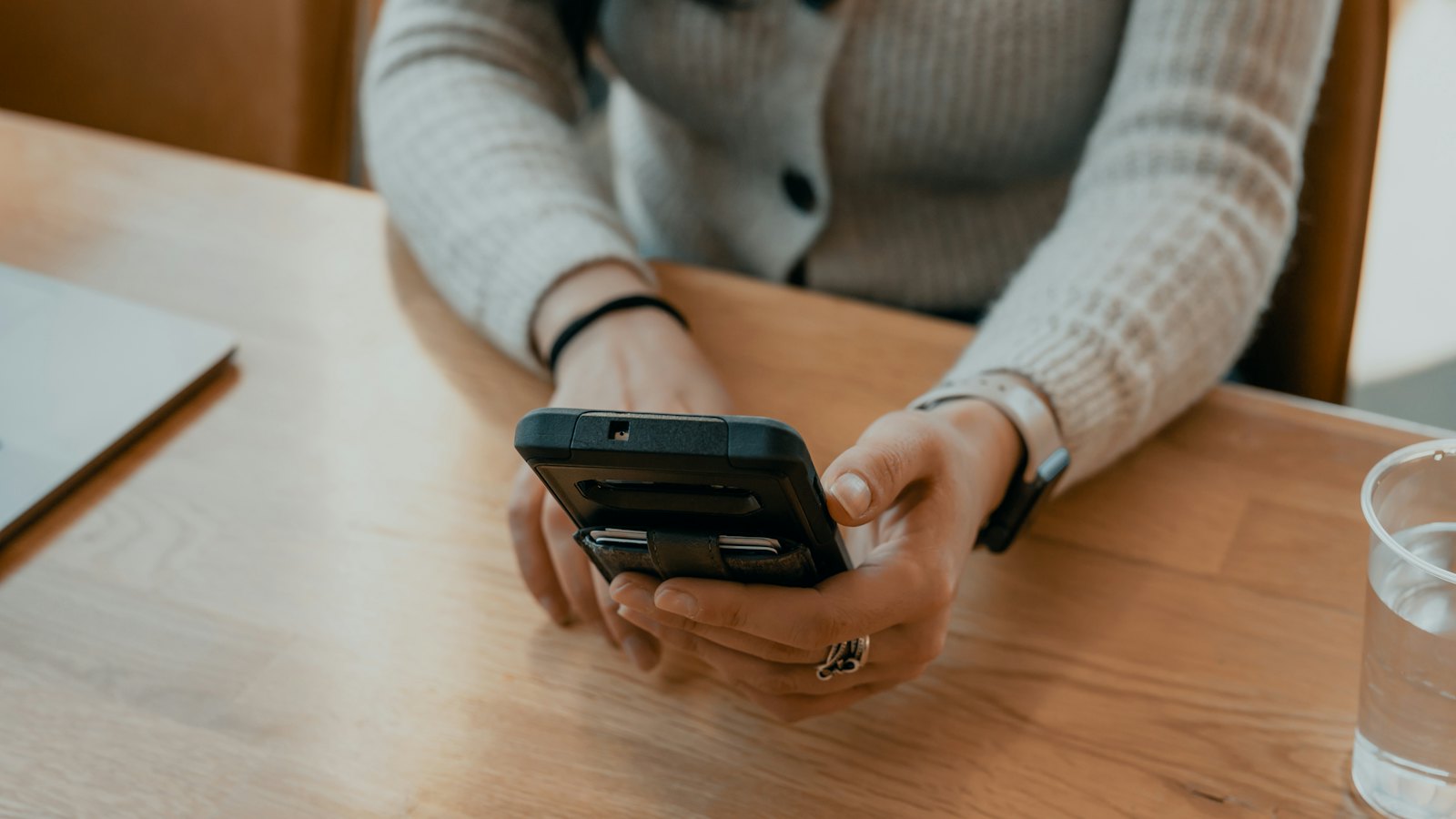 A woman at a wooden table holding a smartphone in both hands