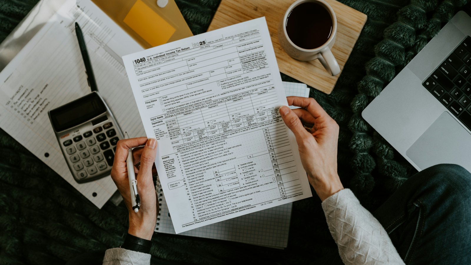 Hands holding a printed form beside a calculator and coffee