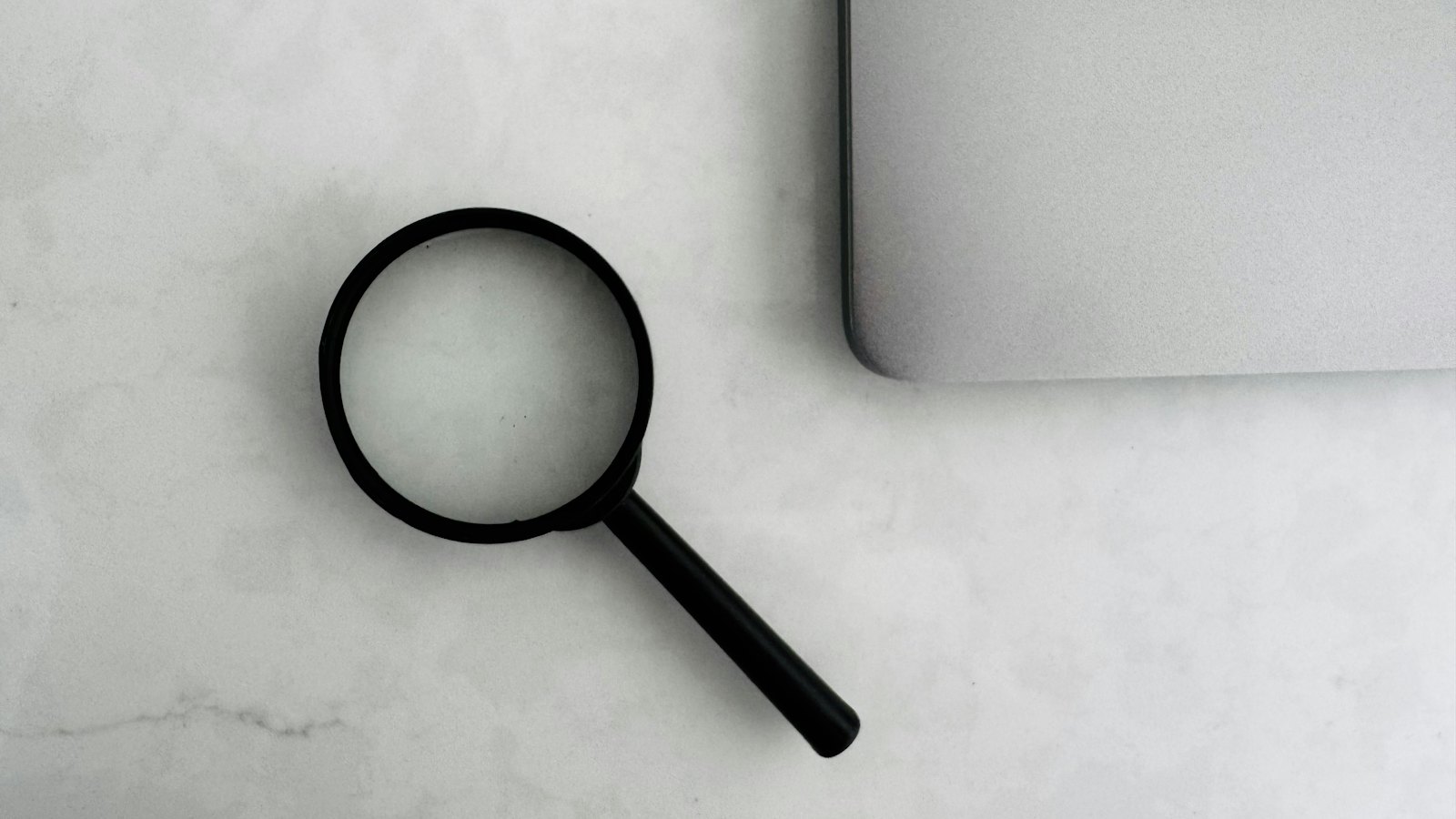 A magnifying glass on a marble table beside a laptop