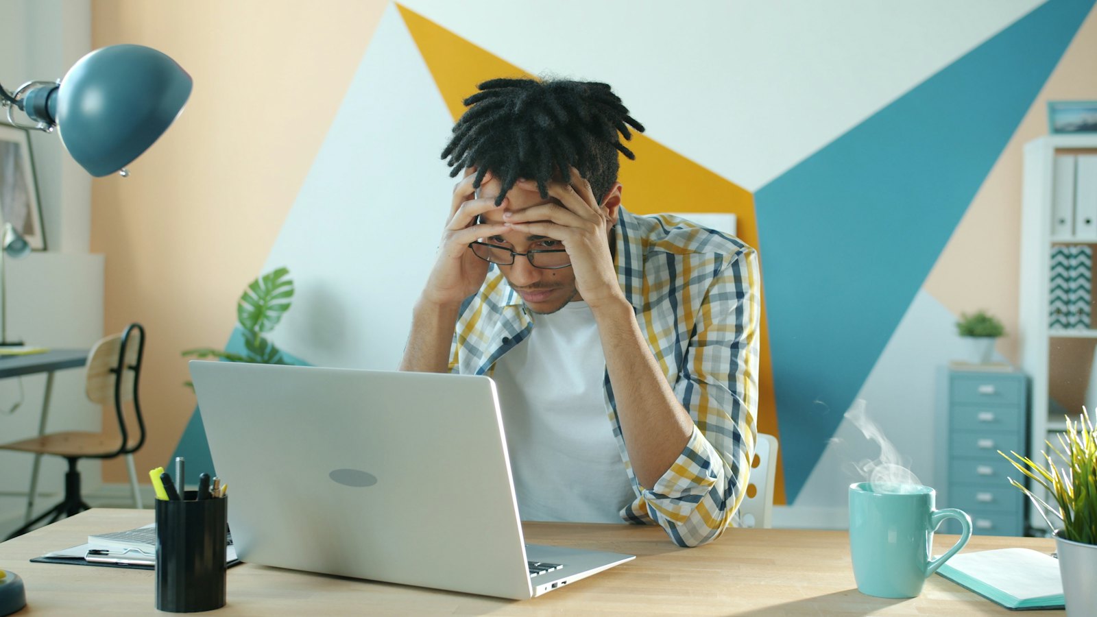 A man at his desk with his head in his hands in front of a laptop