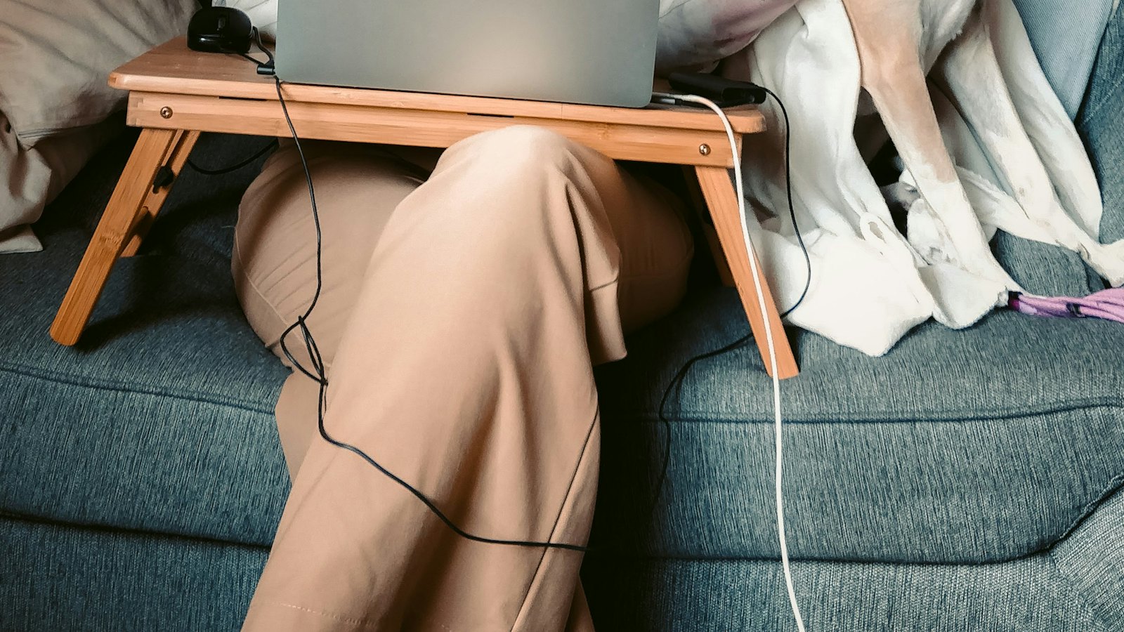 A laptop on a small tray table on someone's lap on a sofa
