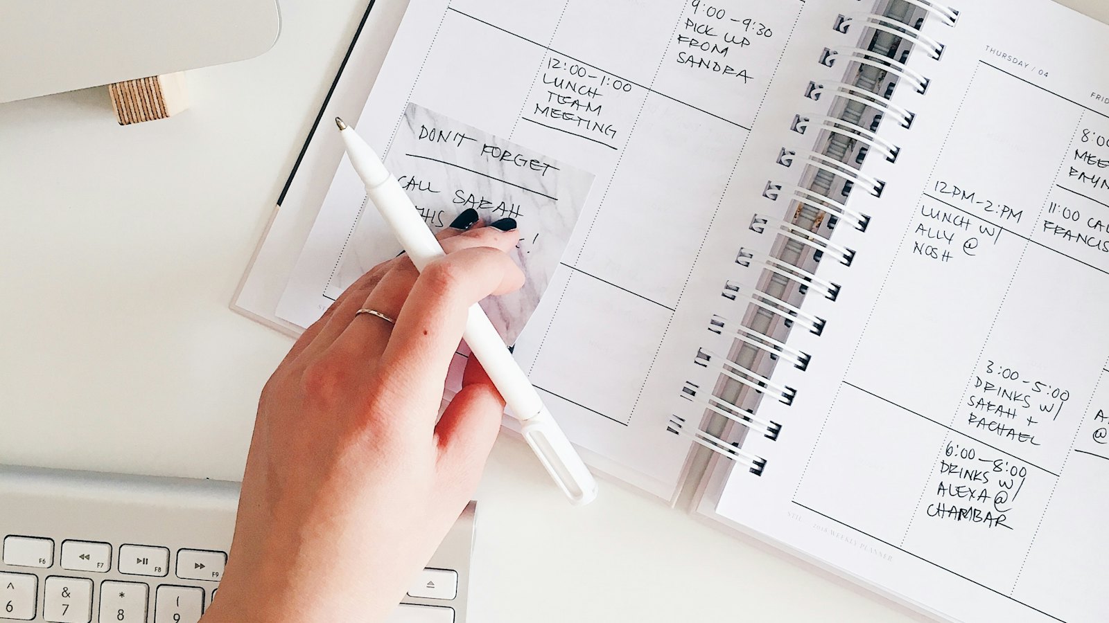 A hand writing in a planner beside a laptop