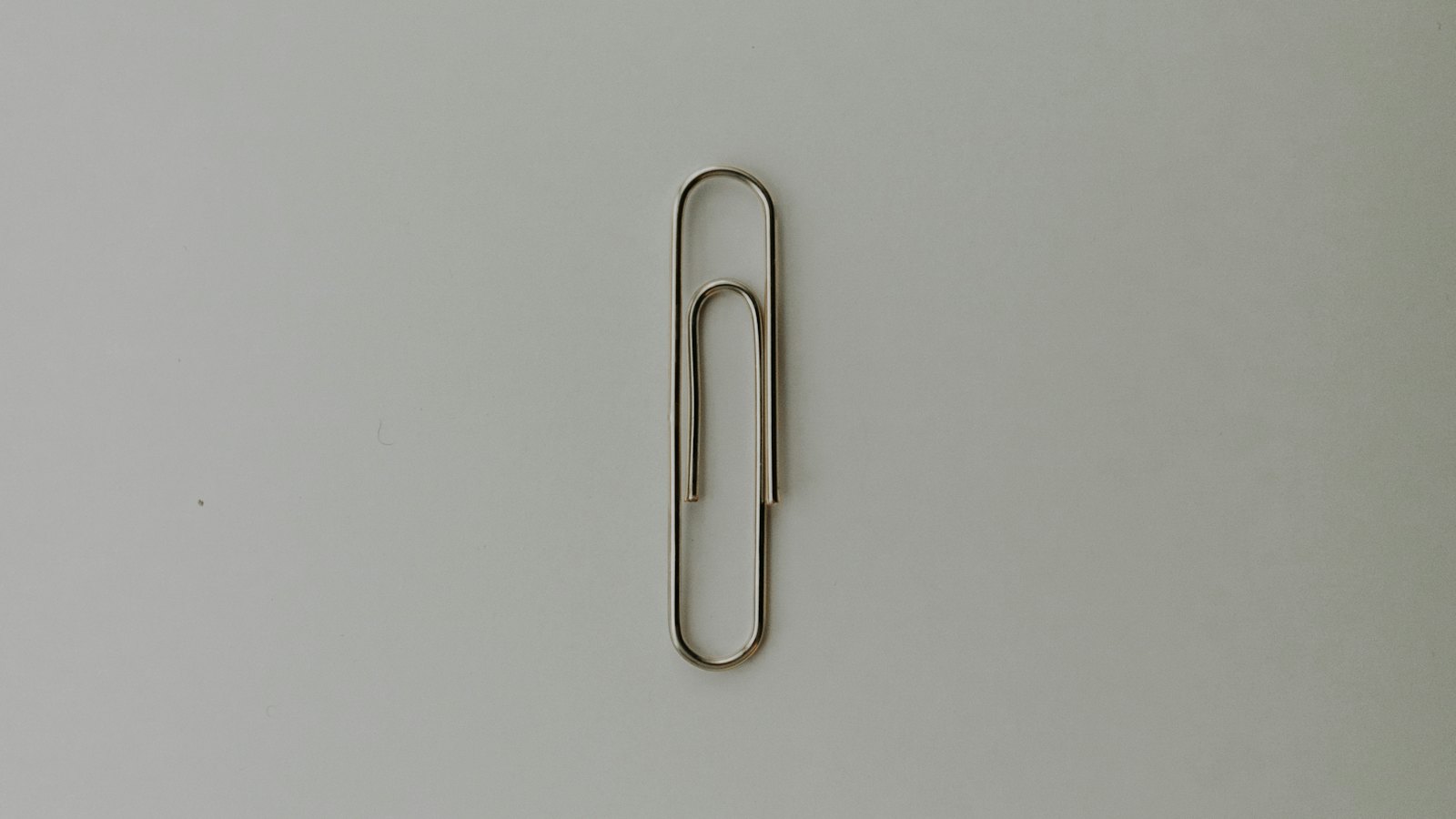 A single metal paper clip on a grey surface