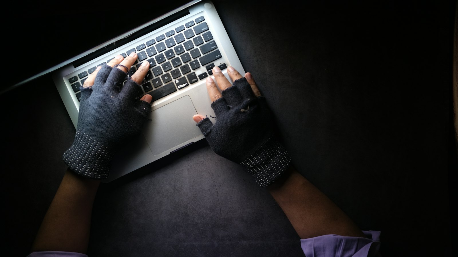 Hands in fingerless gloves typing on a laptop in the dark