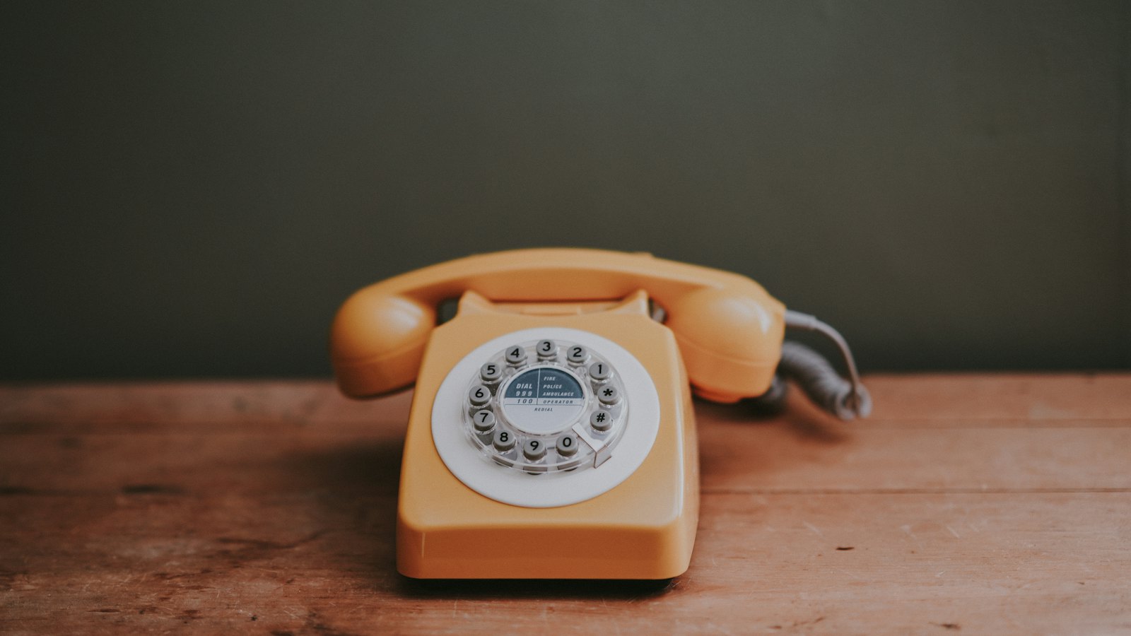 An orange rotary telephone on a wooden table