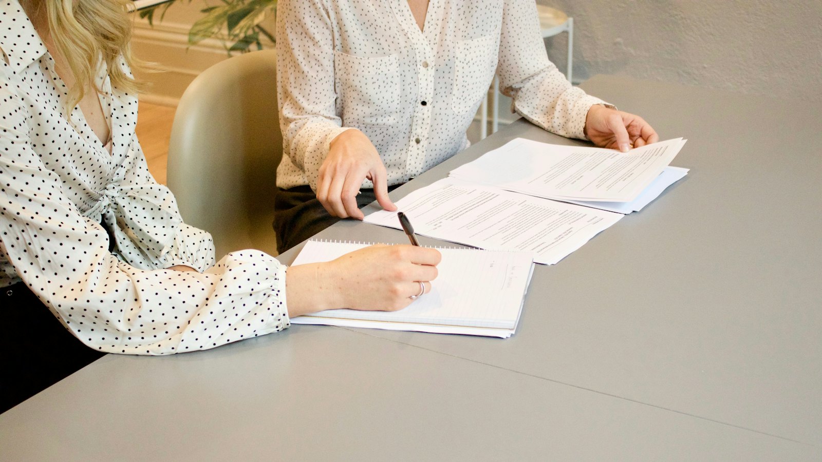 Two women at a desk, one signing a document