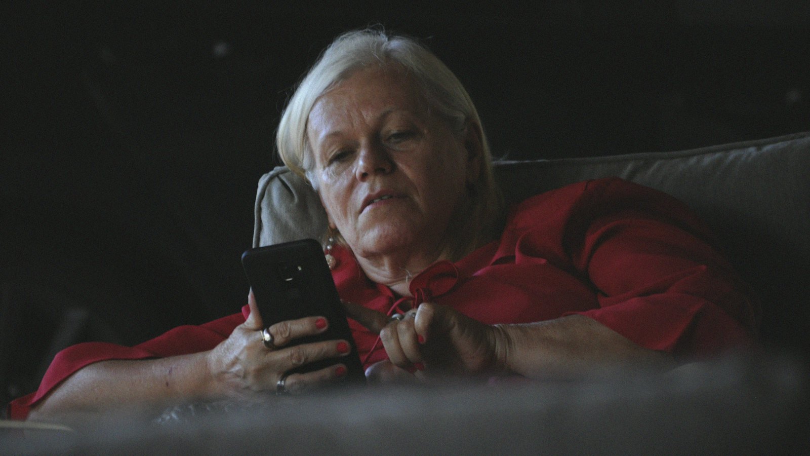 An older woman looking at her phone in a dim living room