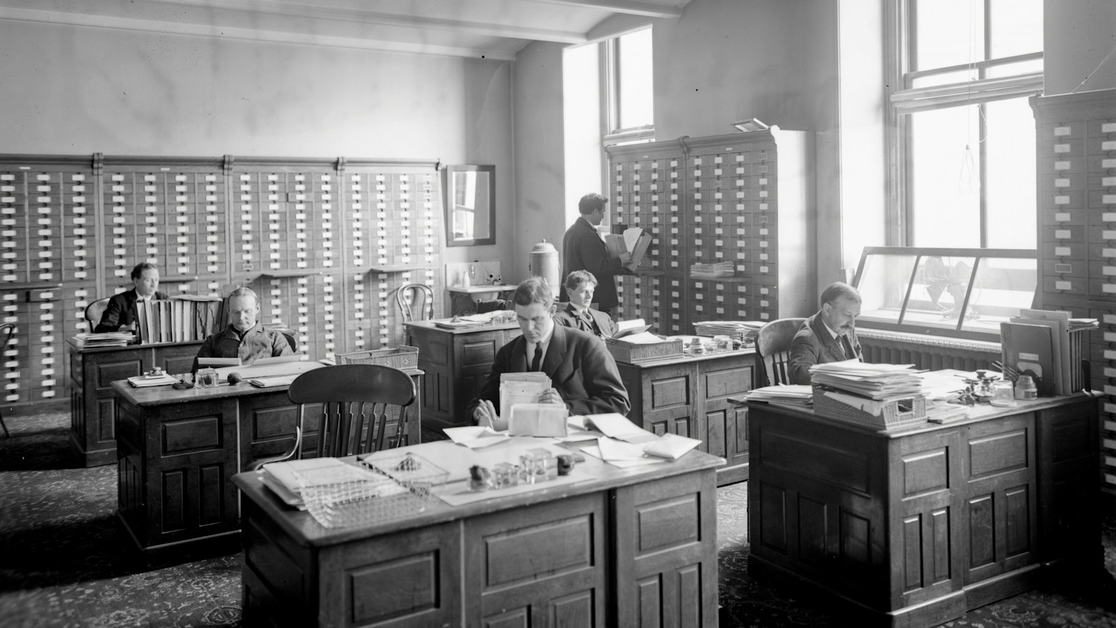 A black and white photo of an old office with rows of desks