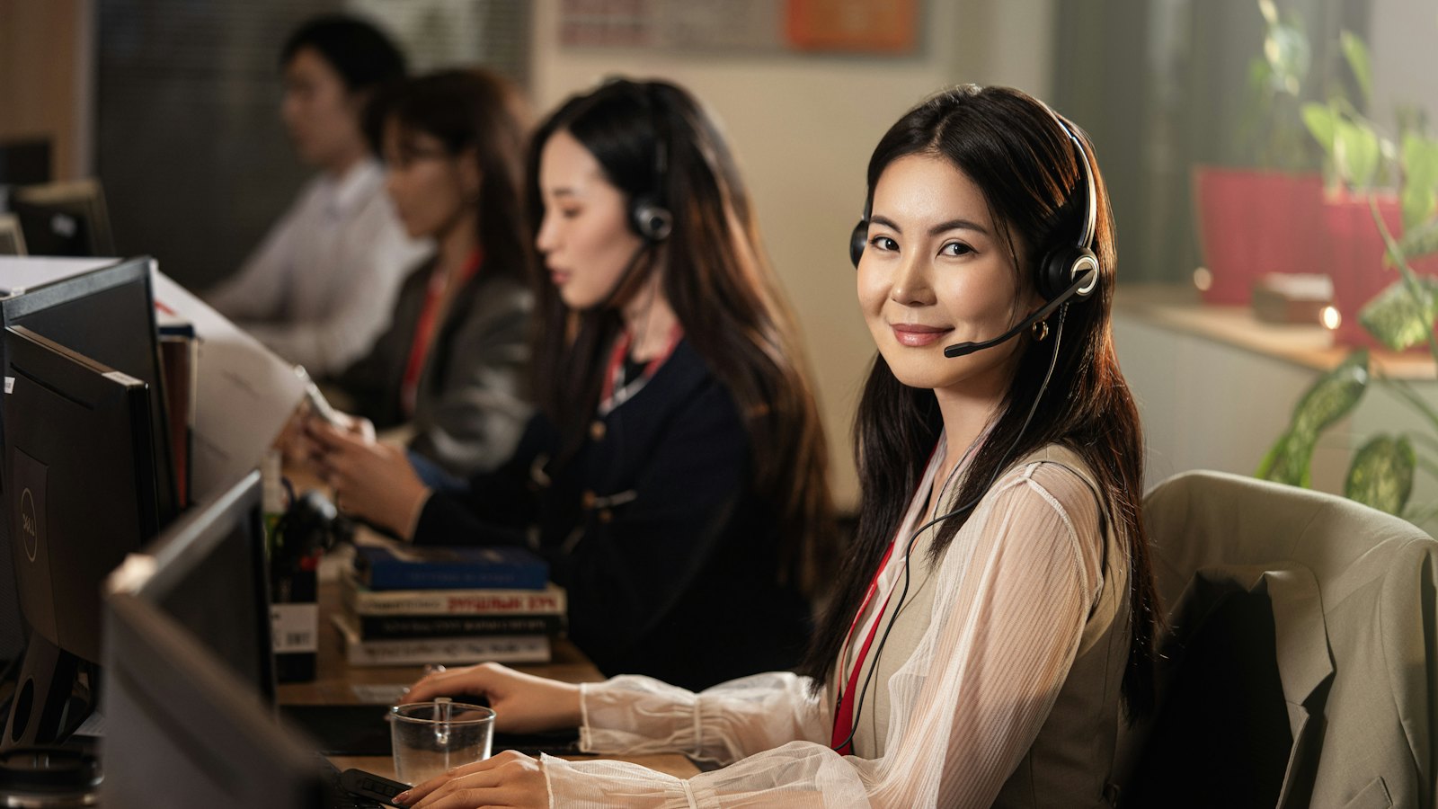 A smiling woman wearing a headset in a busy call centre