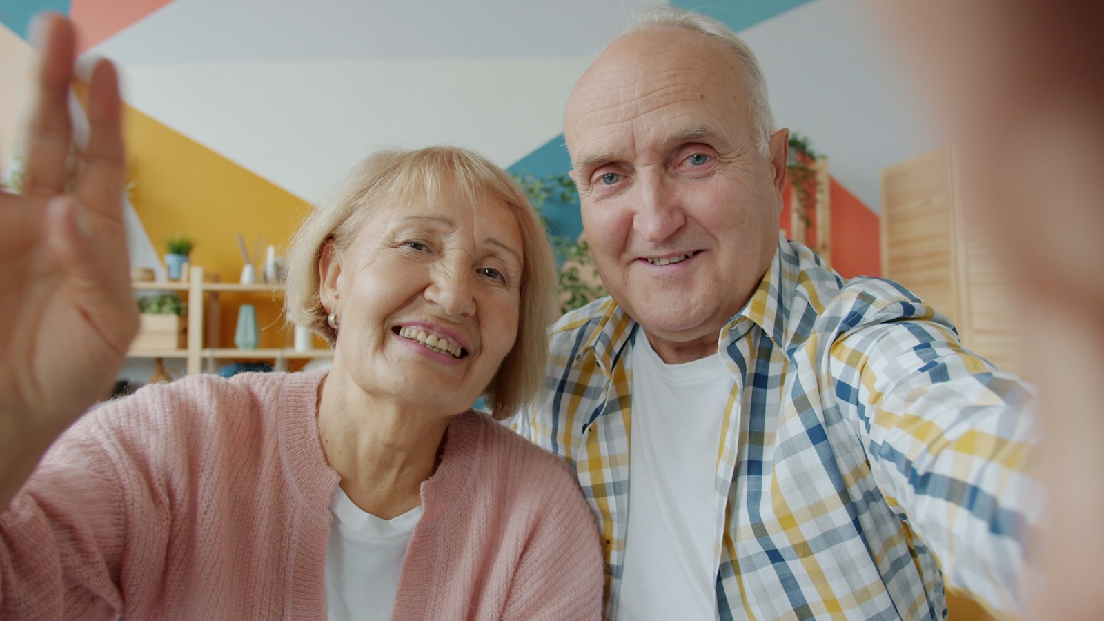 An older couple smiling and waving at the camera during a video call