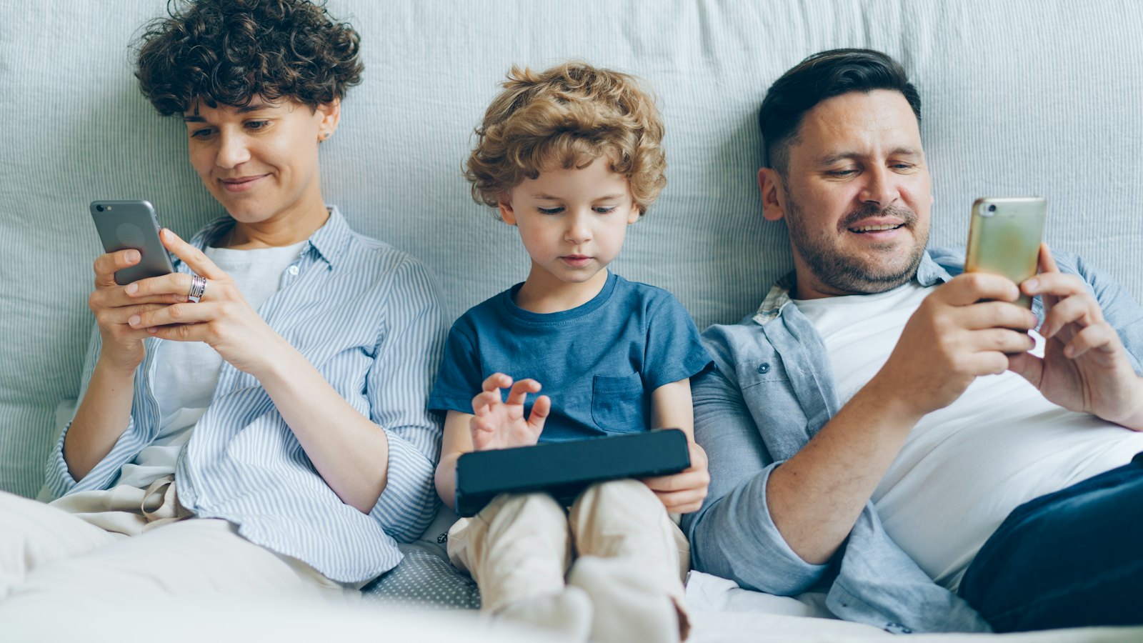 A mother, father and young son on a sofa looking at their phones