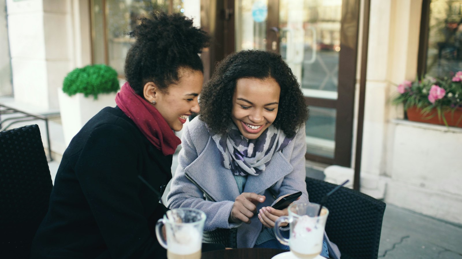 Two friends laughing over a phone in a cafe