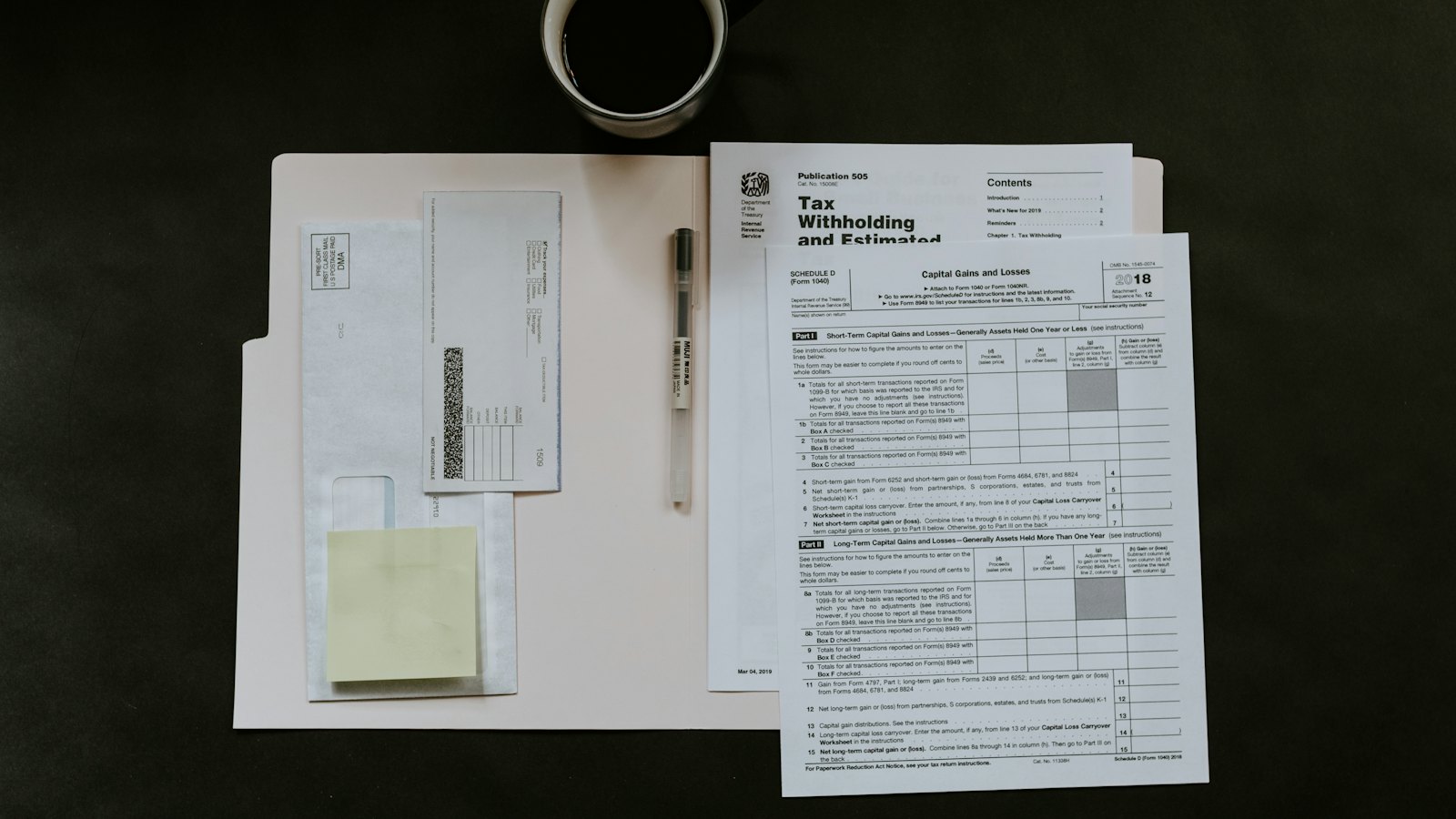 Tax forms, a pen and a coffee cup laid out on a dark desk