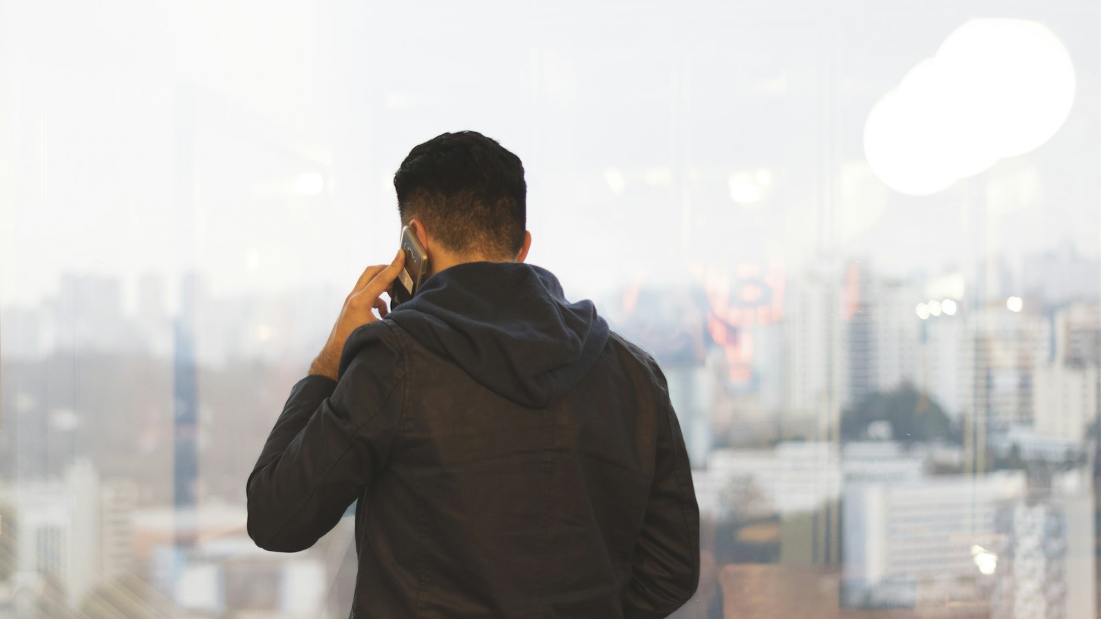 A man seen from behind making a phone call by a window overlooking a city