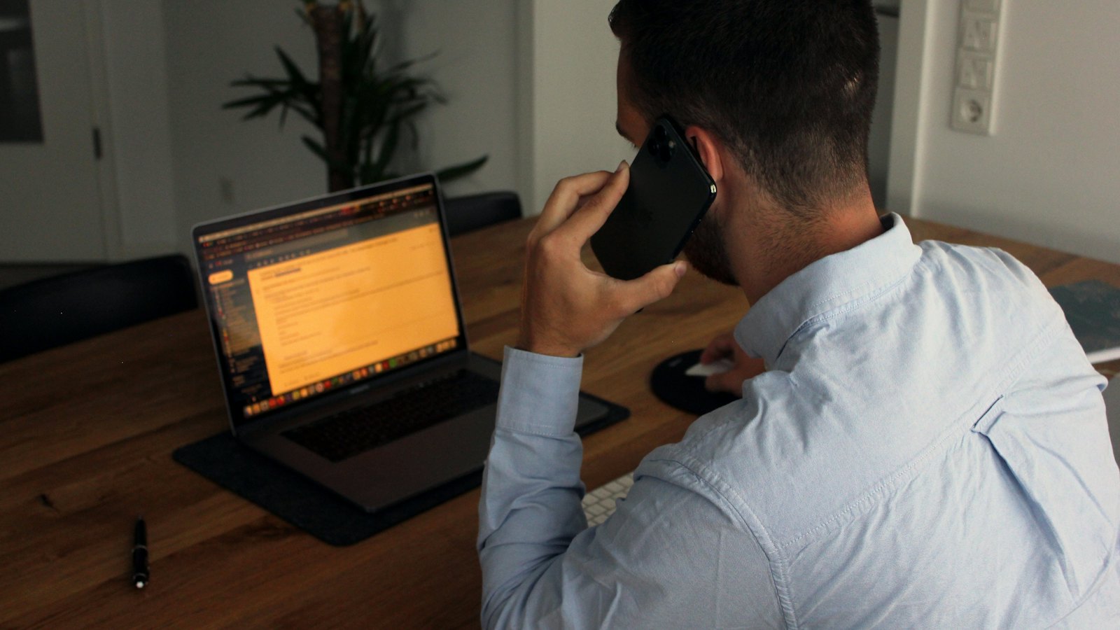 A man on a phone call sitting at a desk in front of a laptop