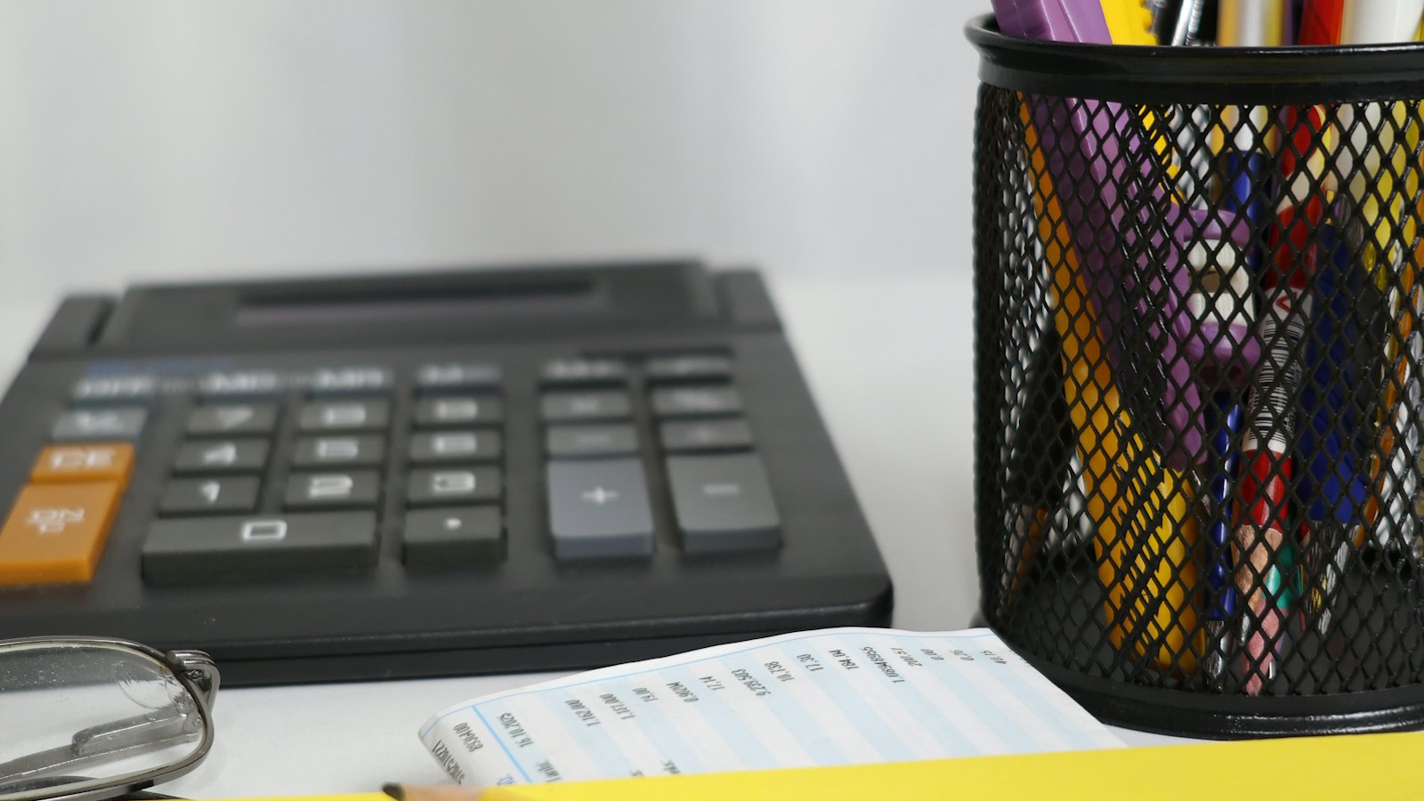 A calculator, a printed invoice and a pen pot on an office desk