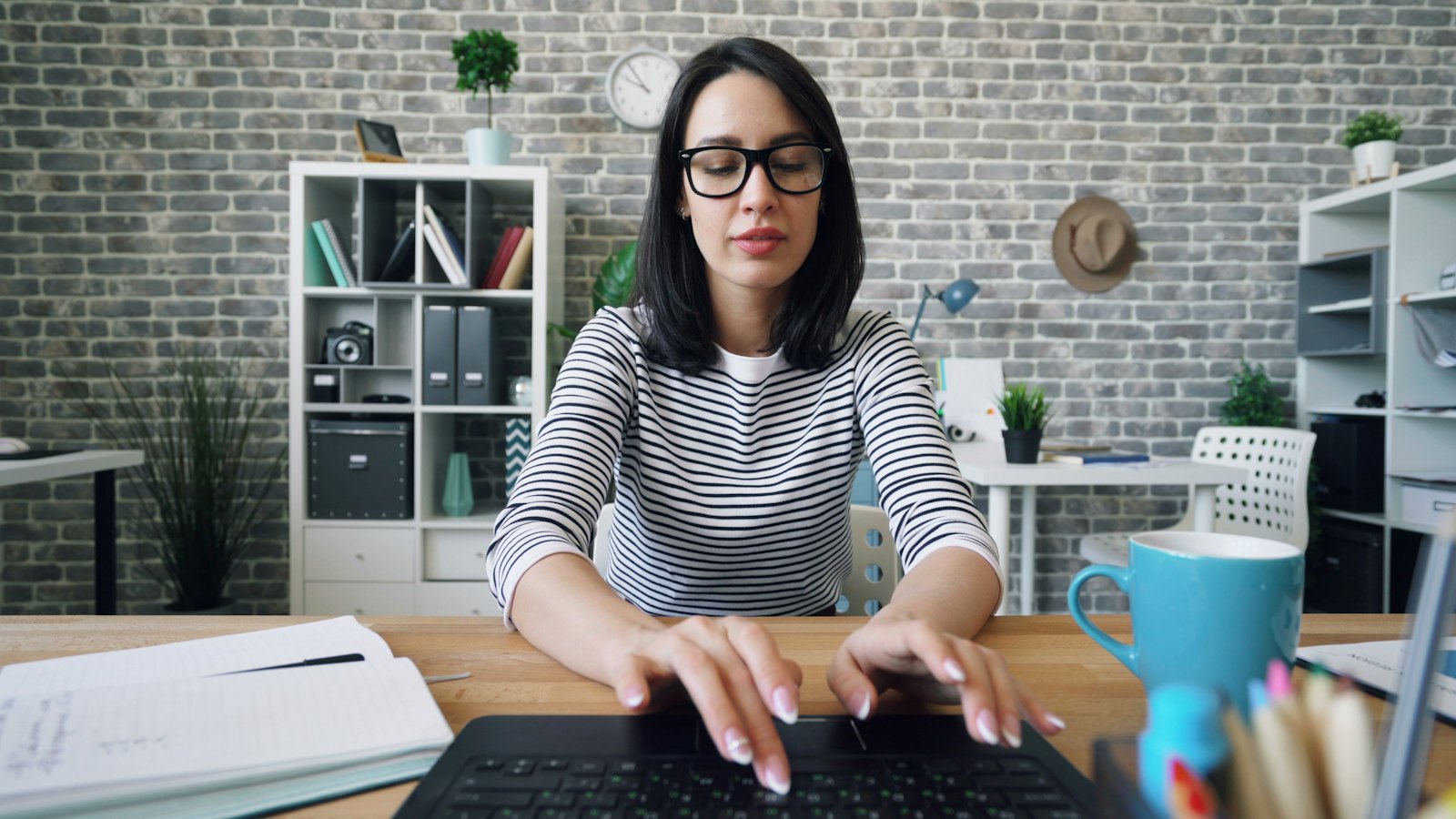 A woman in glasses typing at a desk in an office