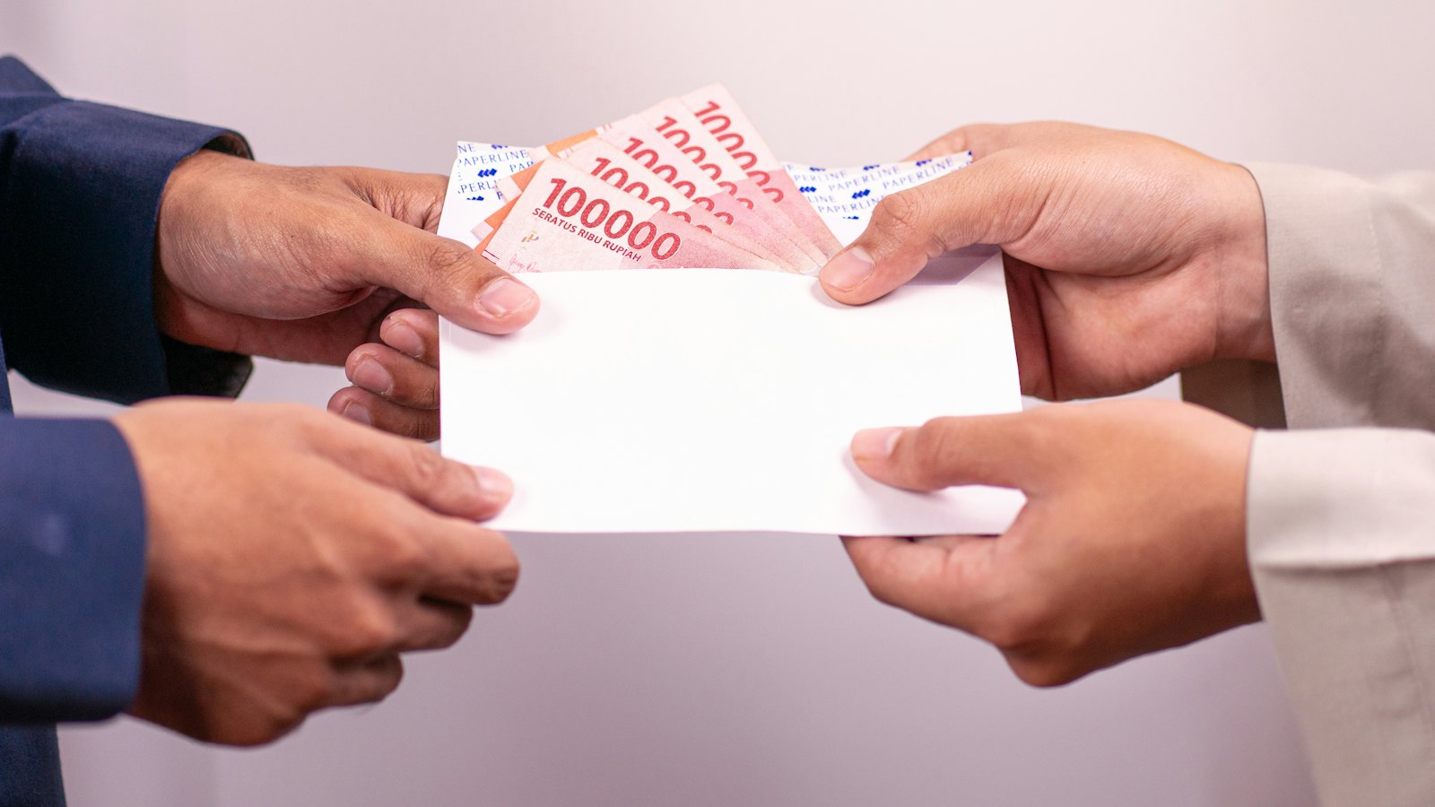One person handing another an envelope of banknotes
