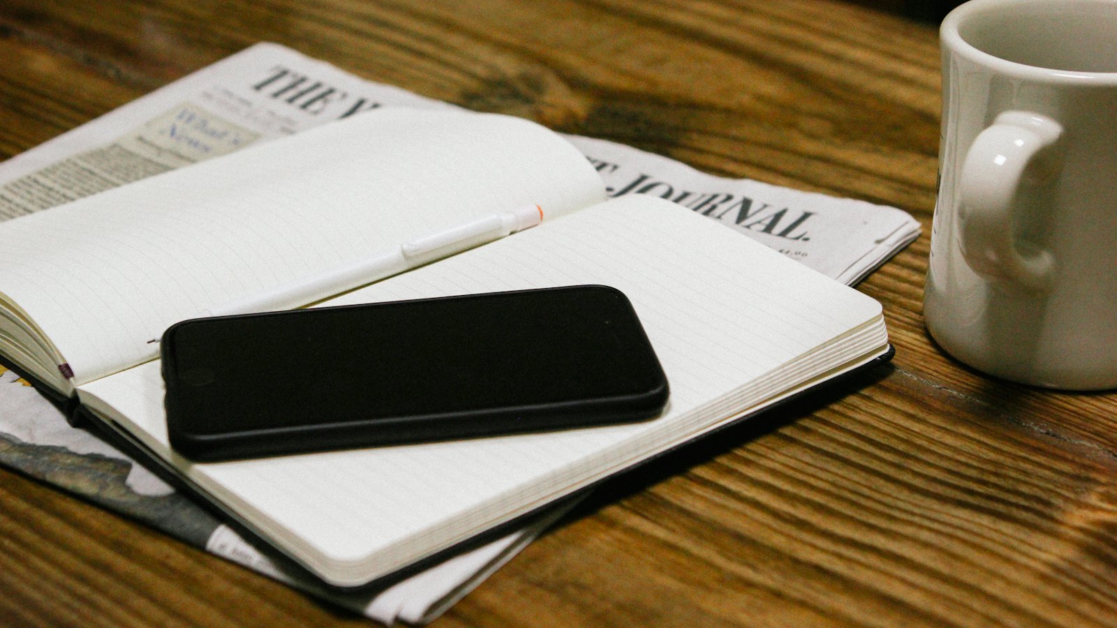 A phone resting on an open notebook beside a coffee cup