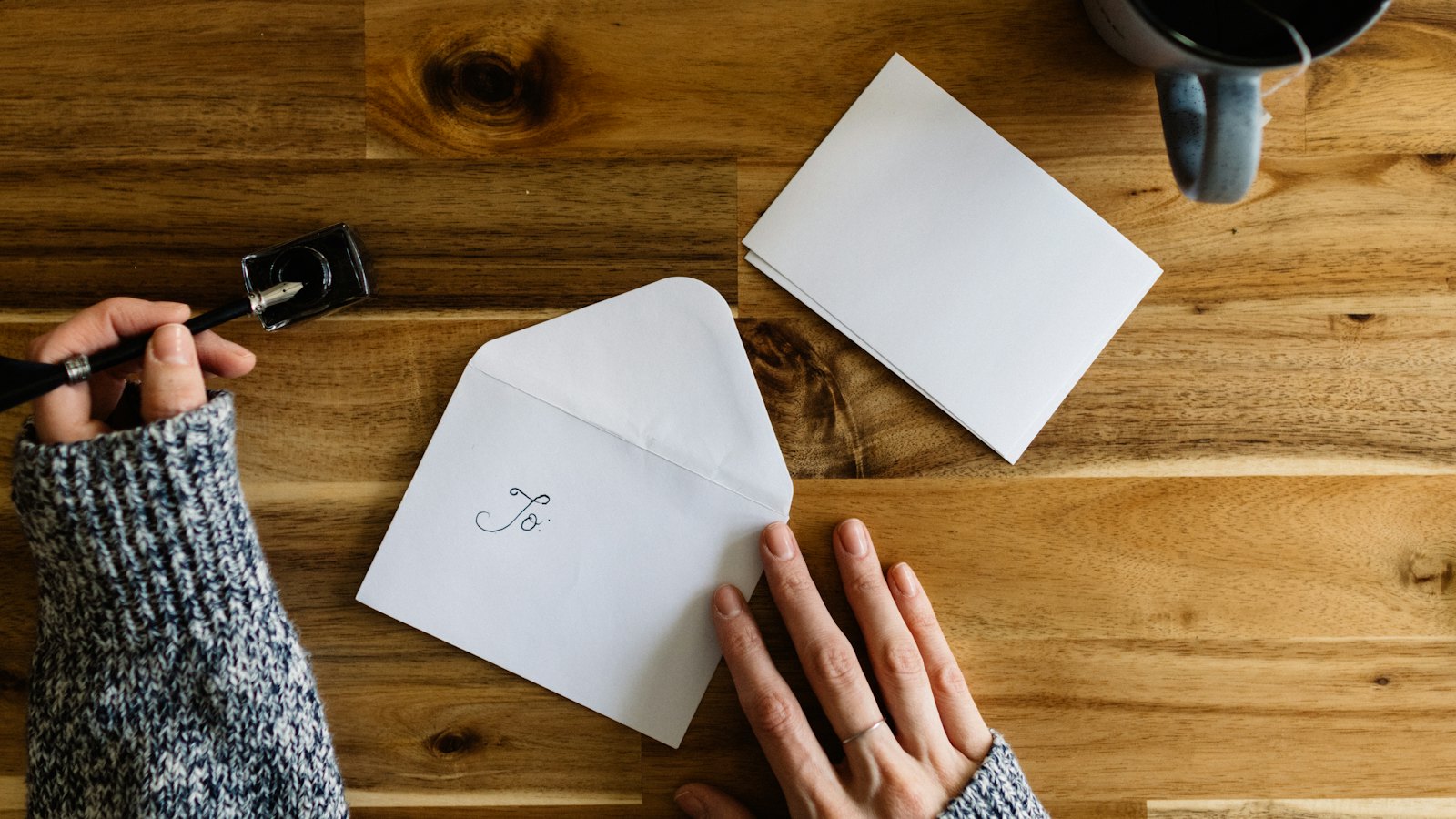 Hands writing a note beside an envelope and a cup of coffee