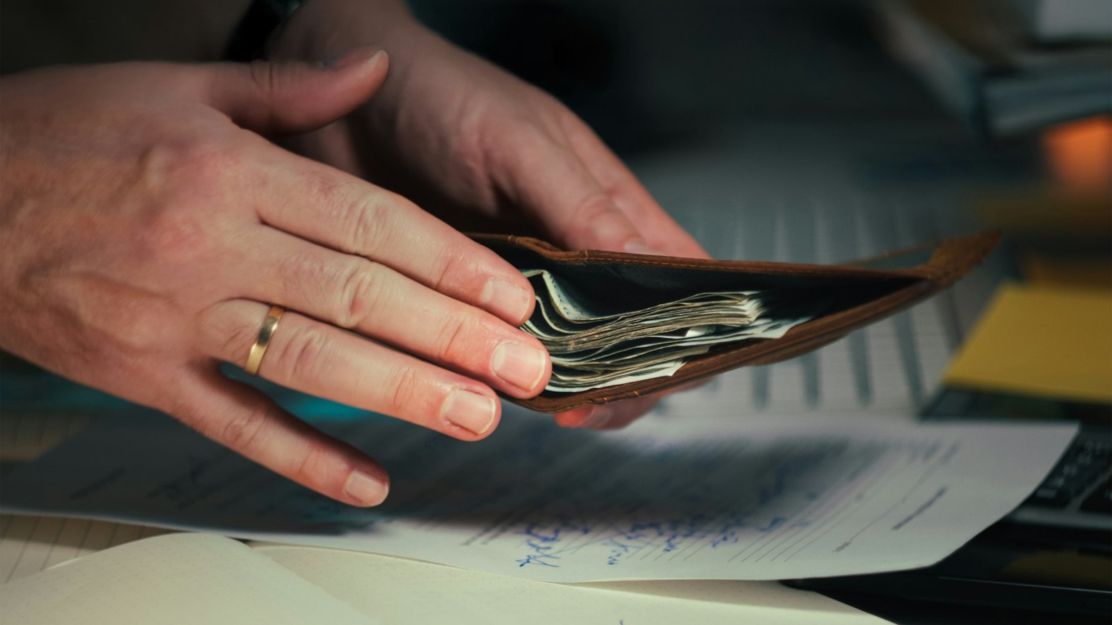 Hands holding cash in a wallet over papers