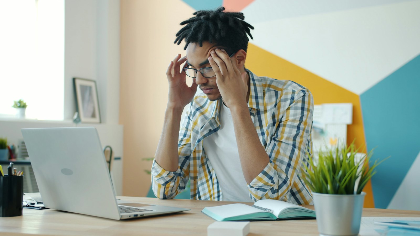 A man holding his head at a desk with a laptop