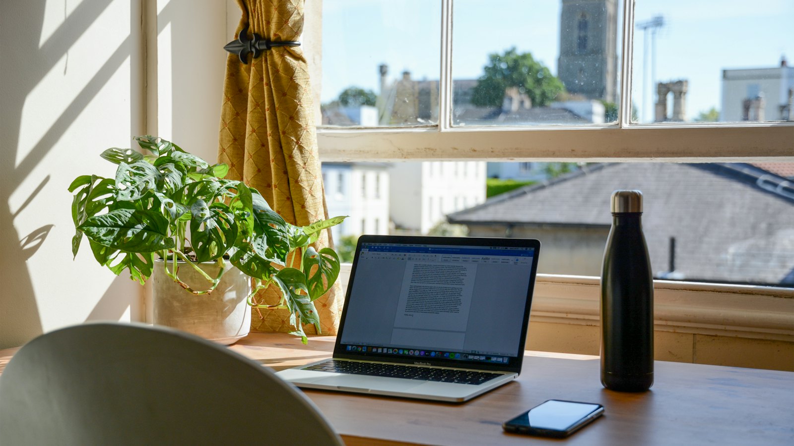 A laptop and phone on a desk by a sunny window