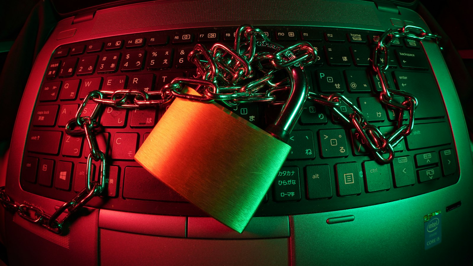 A laptop keyboard wrapped in a chain and padlock under red and green light