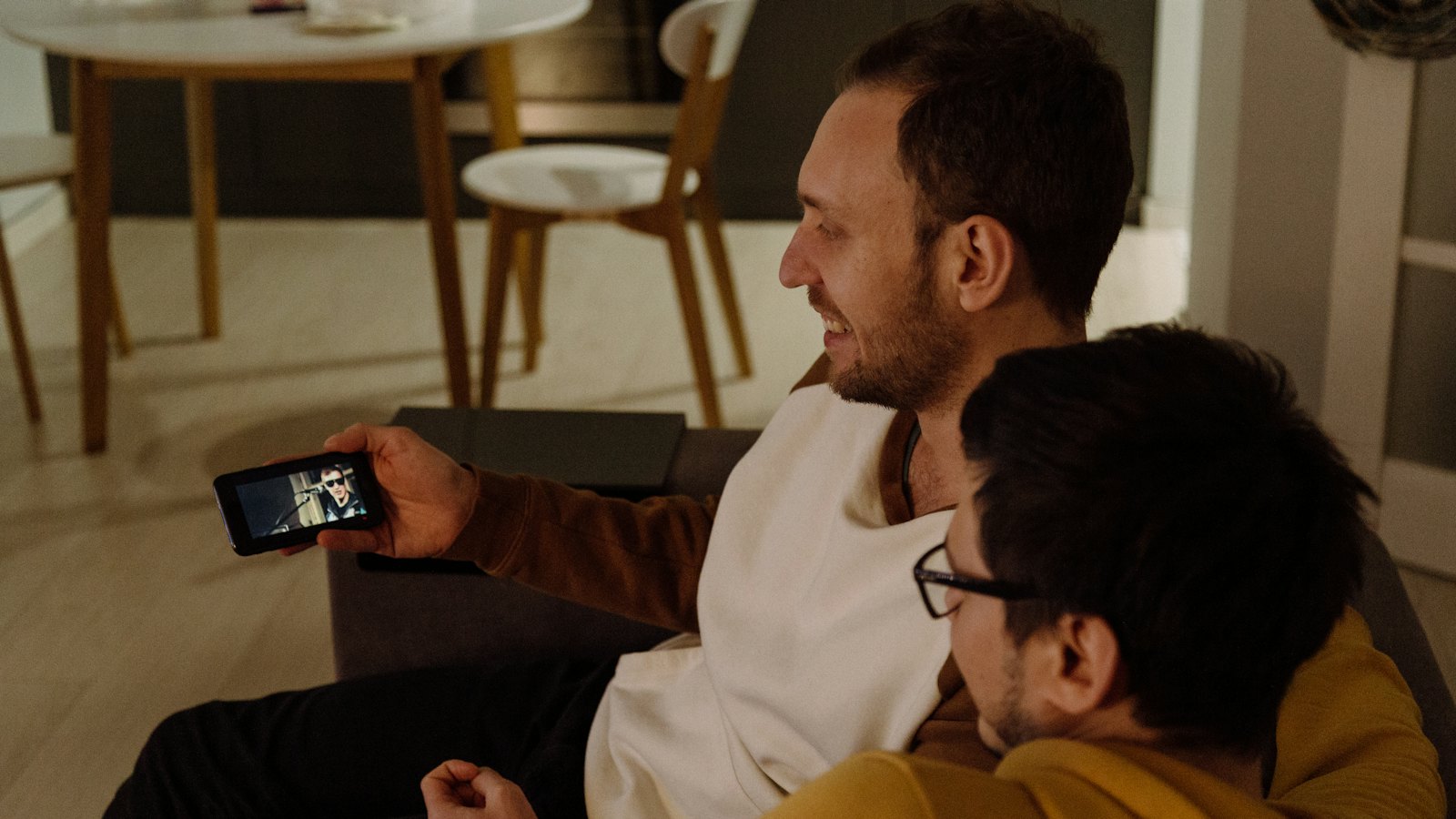 Two men looking at a phone on a sofa
