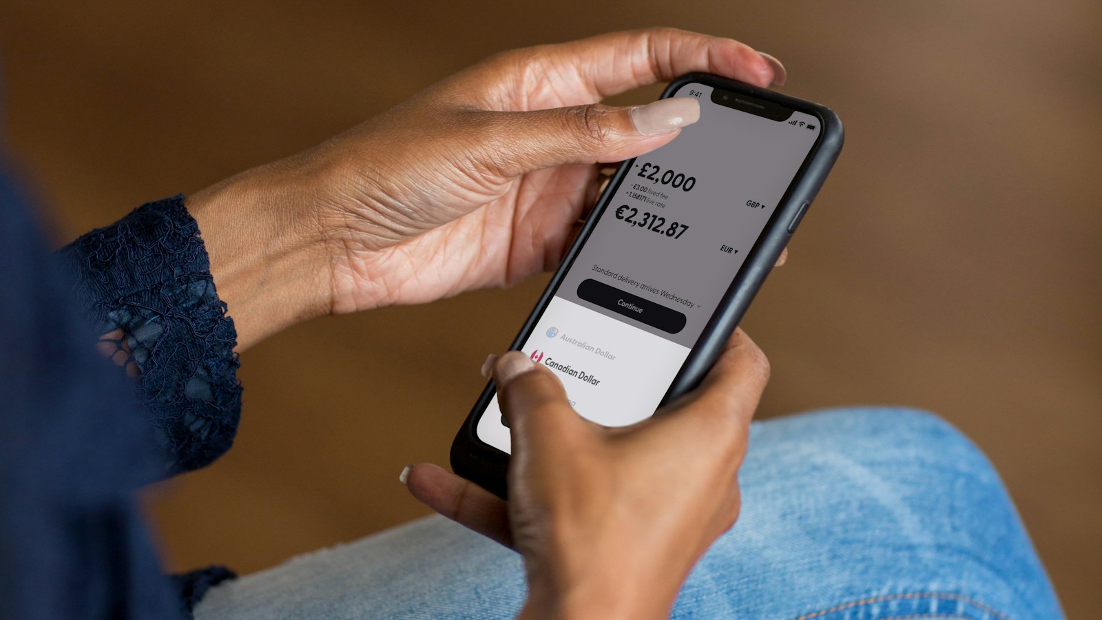 A woman holding a phone showing a money transfer screen