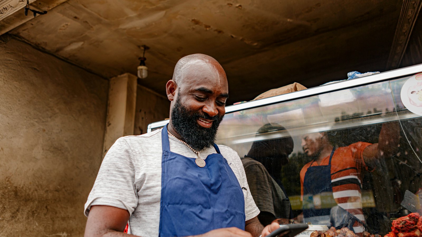 A smiling food vendor checking his phone at his stall