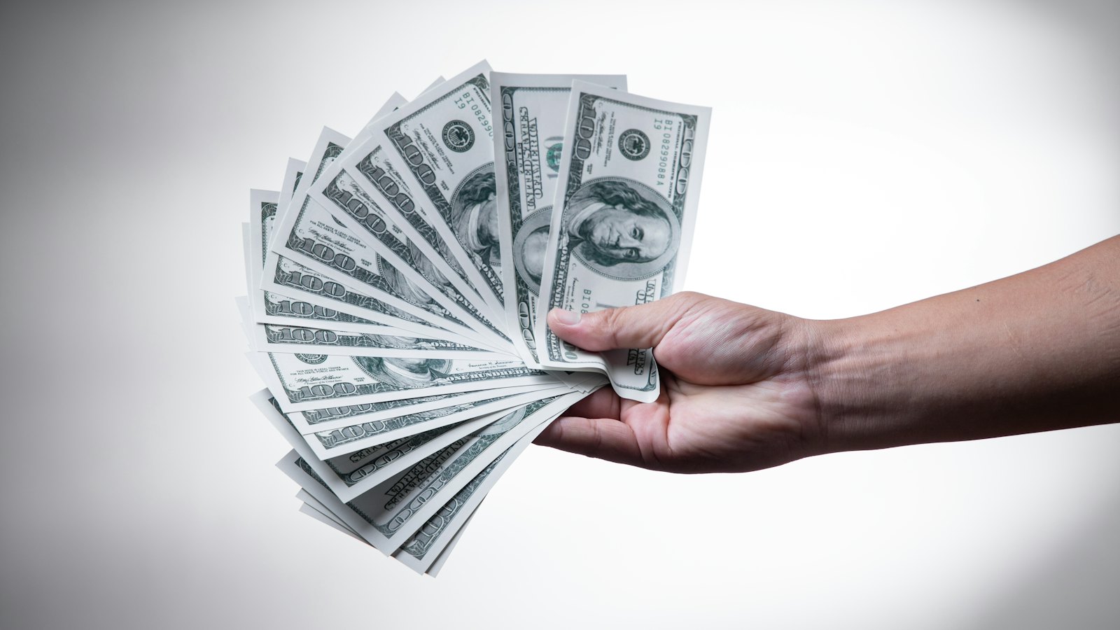 A hand holding out a fan of banknotes
