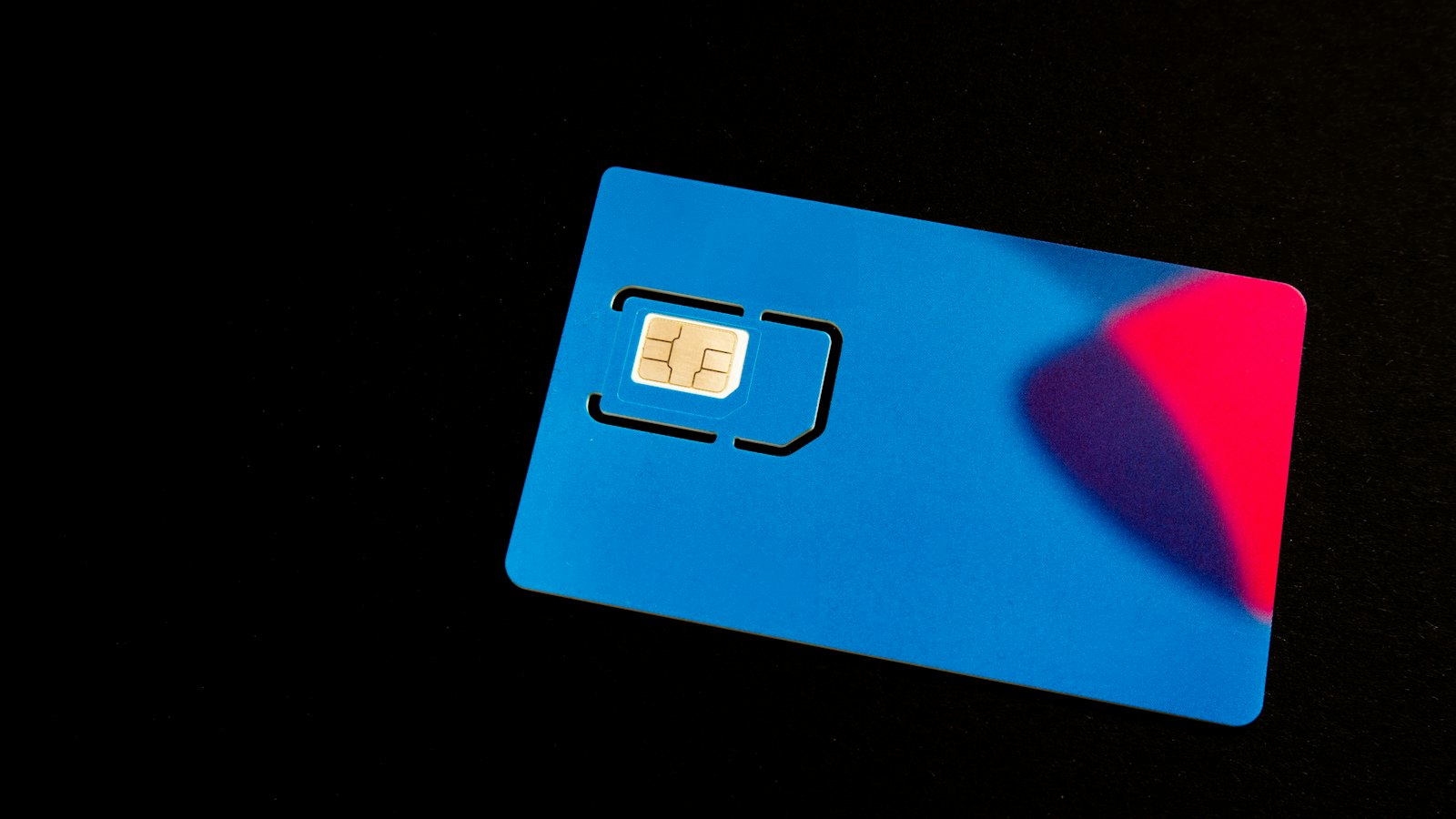 A SIM card in its blue plastic holder on a dark surface