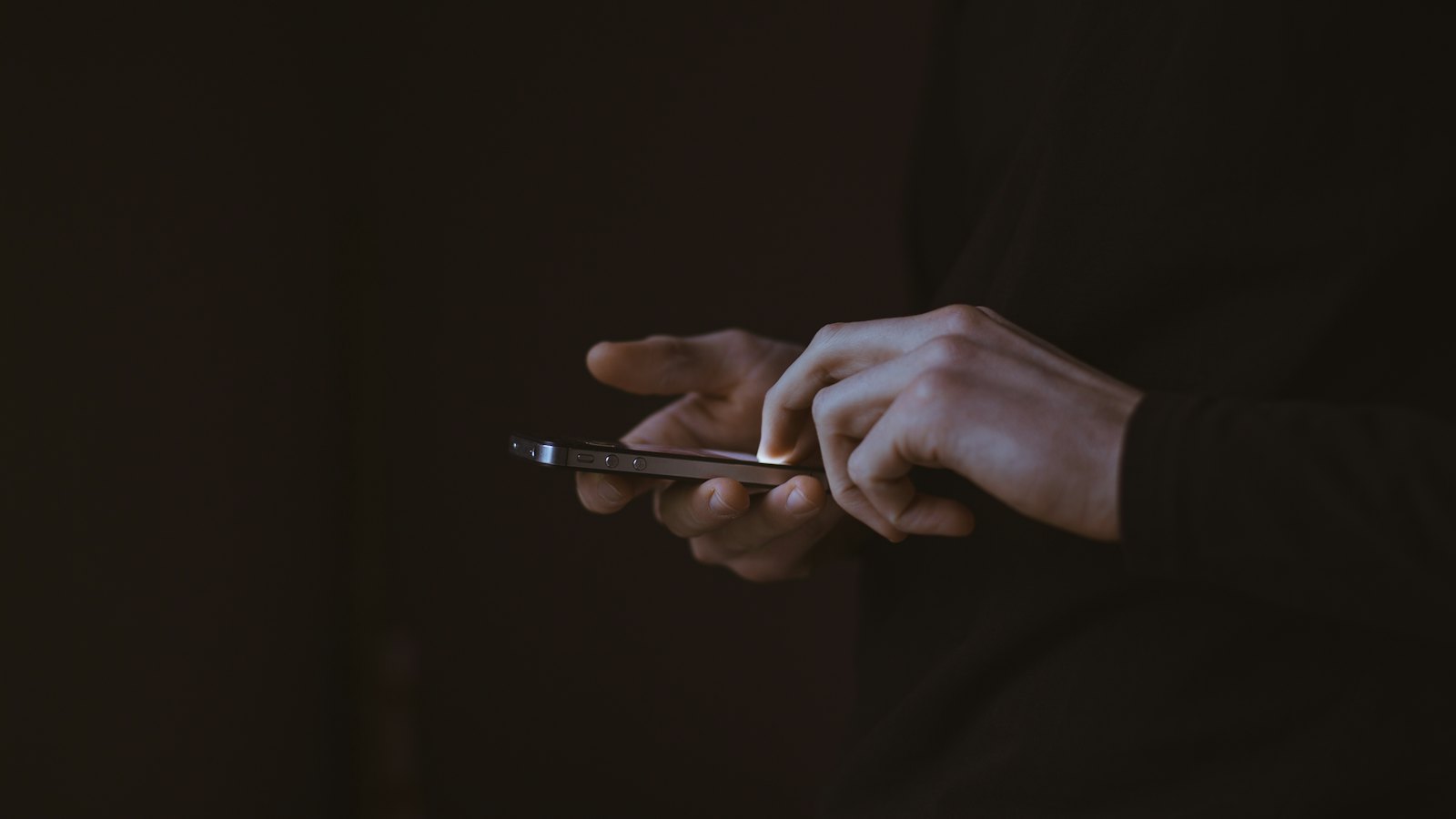 Hands holding a softly lit smartphone in a dark room