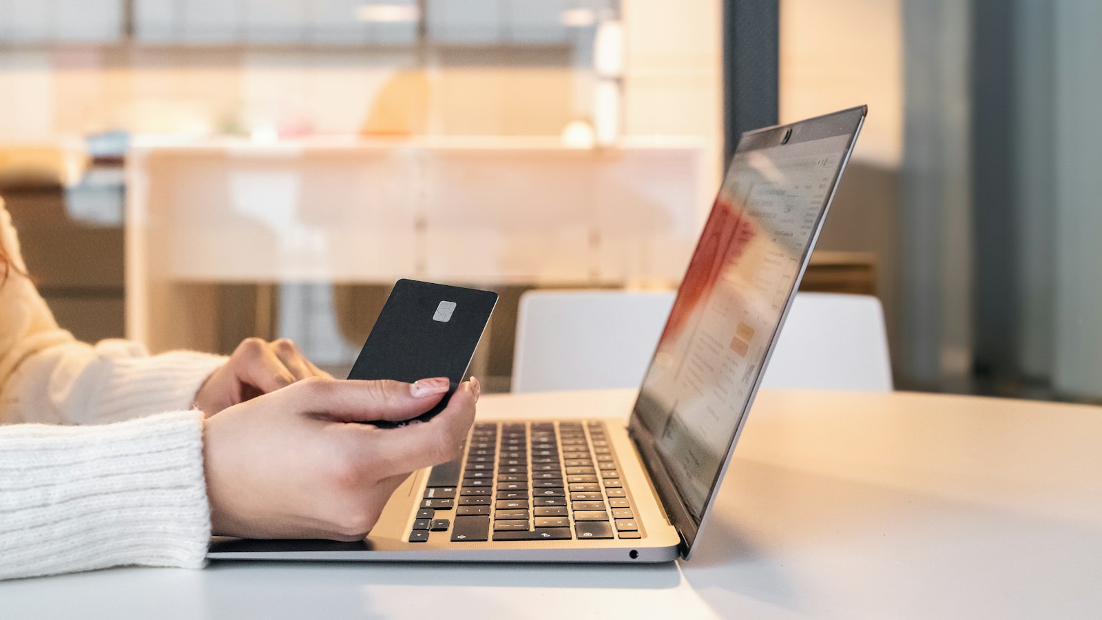 A person holding a bank card next to an open laptop, about to pay online