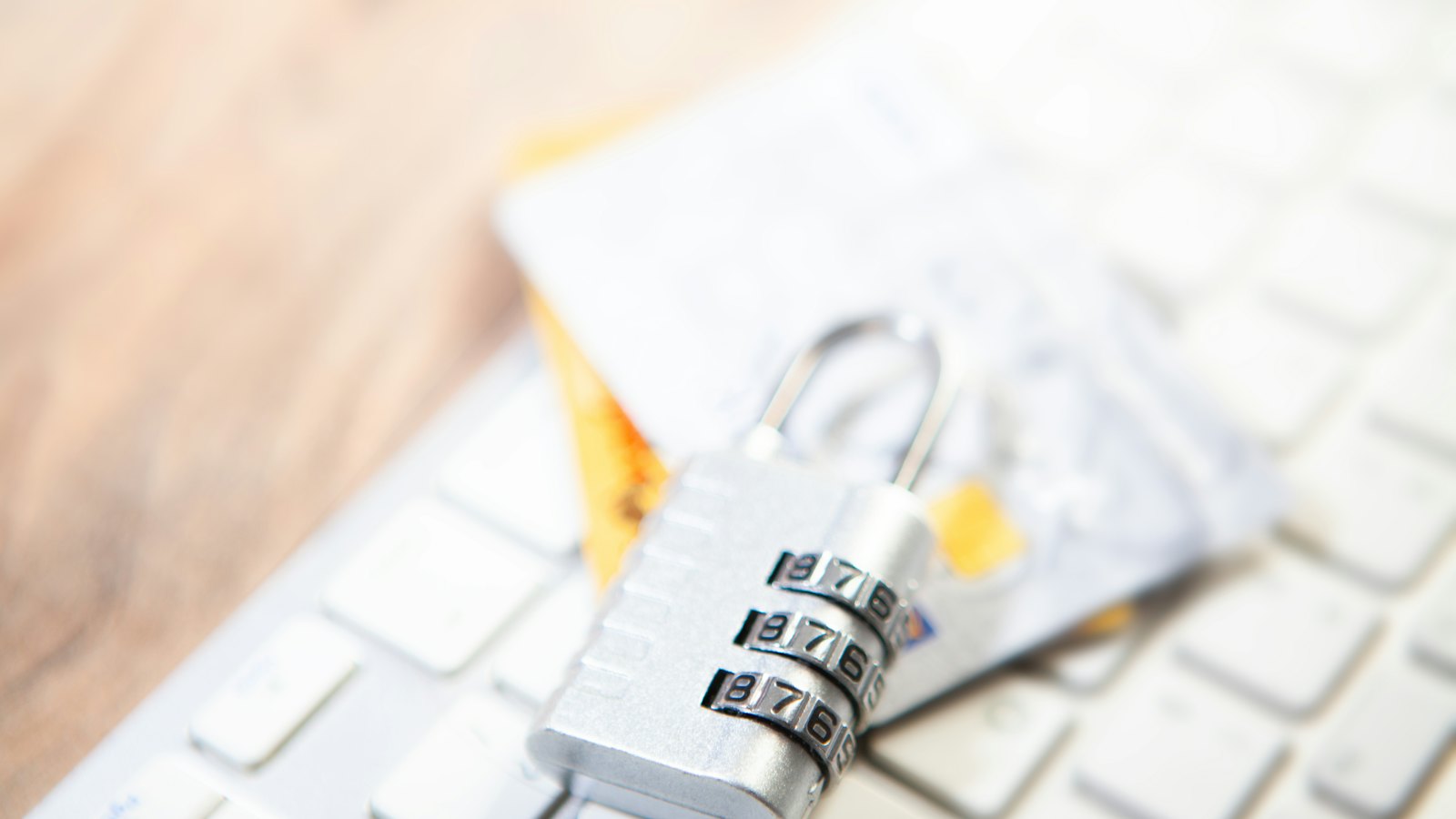 A combination padlock resting on a laptop keyboard beside bank cards