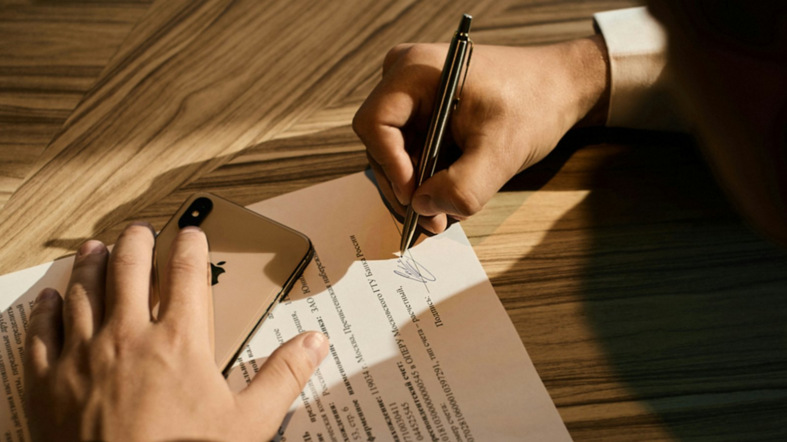 A person signing a document while holding a phone