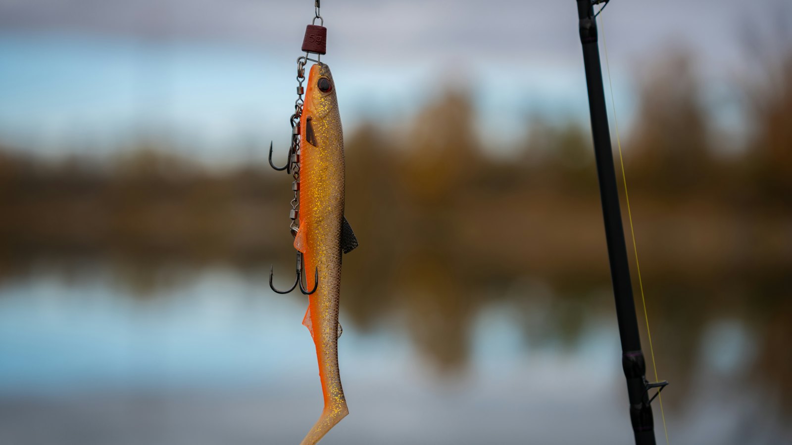 A realistic fishing lure hanging from a fishing rod above a lake