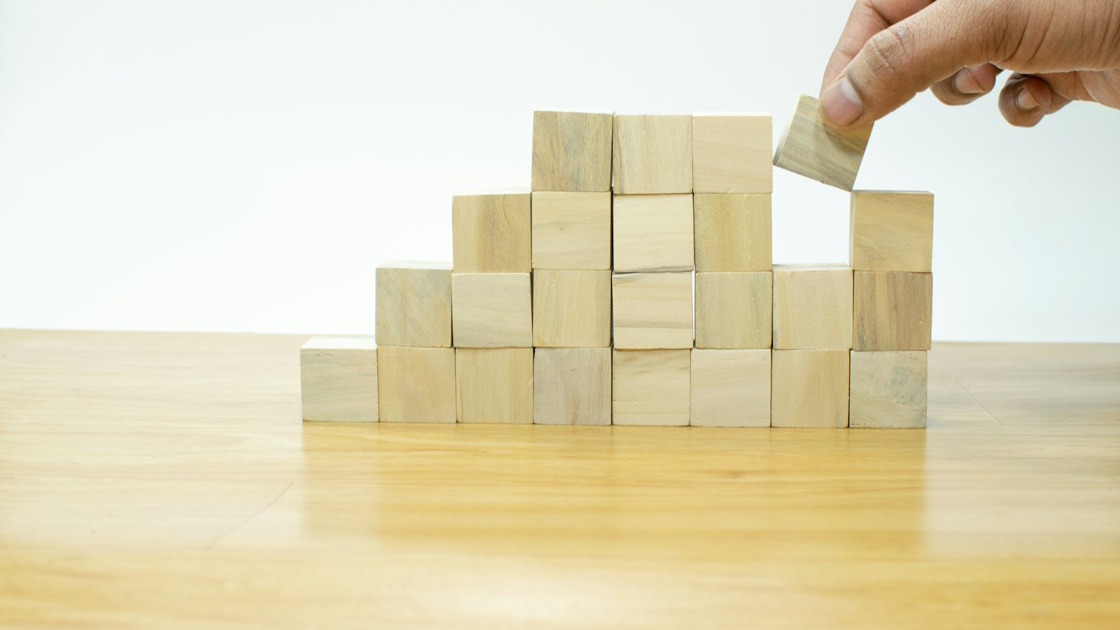 A hand placing a wooden block on a stacked pyramid