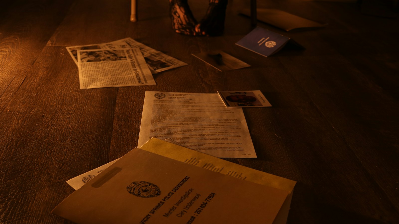 Printed documents and photographs spread across a dark wooden floor