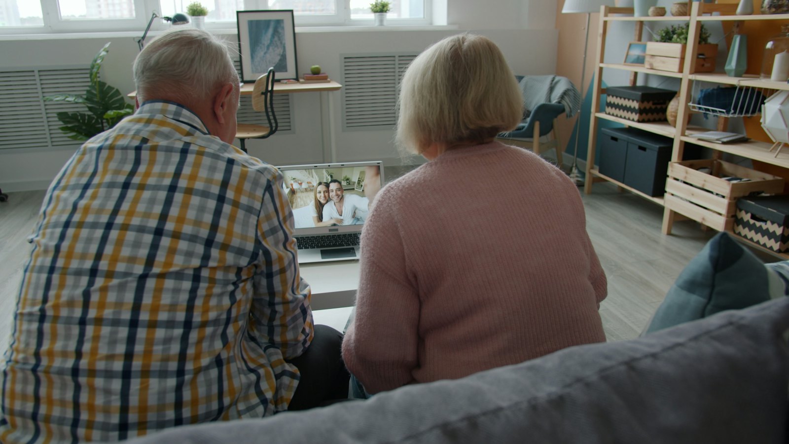 An older couple sitting together watching a video call on a laptop